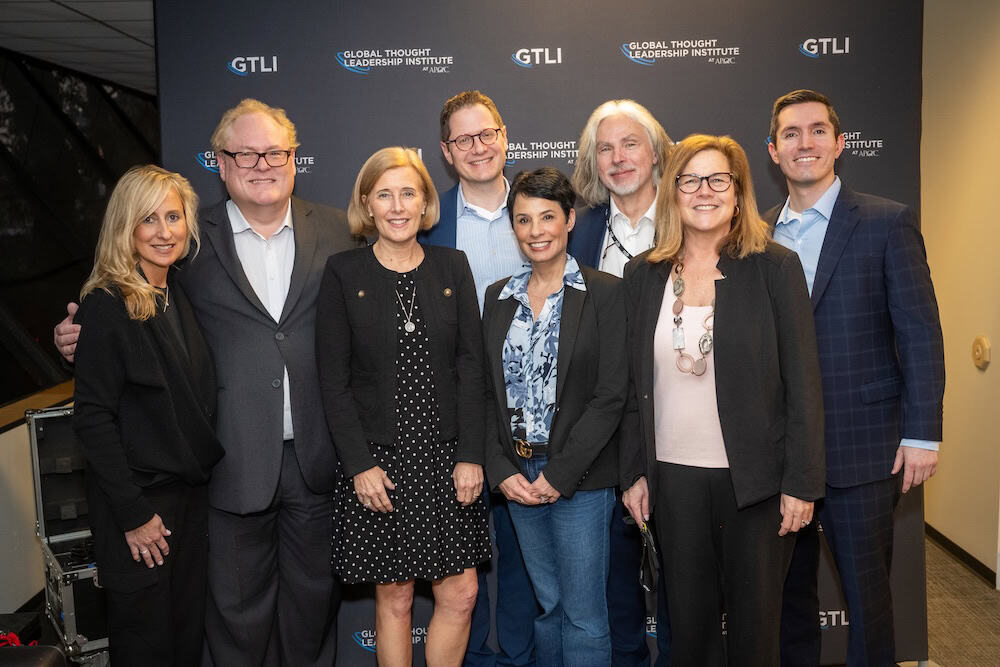 'n Groep van vier vroue en vier mans poseer saam, glimlaggend, voor 'n agtergrond met die "Global Thought Leadership Institute" en "GTLI" logo's. Almal dra sake- of sake-informele klere.